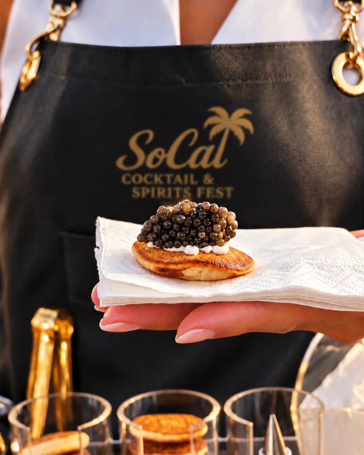 A caviar blini held in front of a SoCal Cocktail & Spirits Fest apron