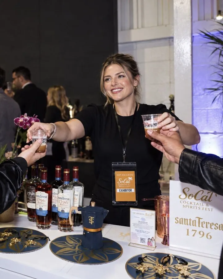 A Santa Teresa exhibitor smiling as she hands tastings to guests