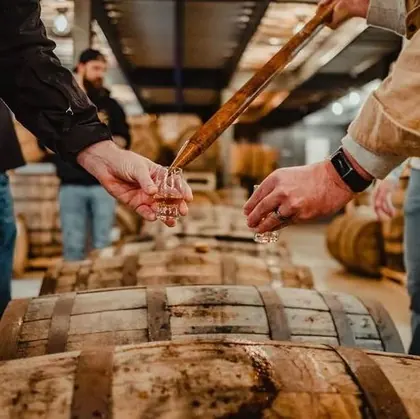 A person pouring spirits from a barrel into a tasting glass